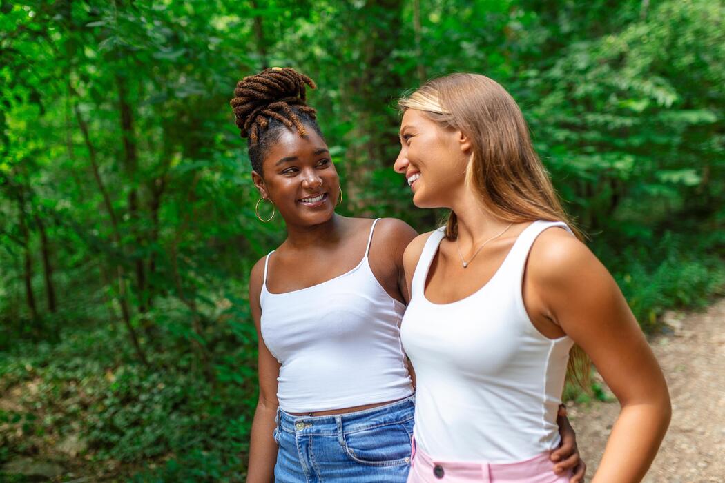 Young smiling women walking and talking while looking at each other outdoor - Studio Psiché